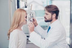 Health care, medicine, eye sight and technology concept. Side profile photo of brunet bearded optician checking blond`s lady patient intraocular pressure at physicians eye clinic