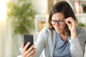 Adult woman with eyesight problems reading phone at home