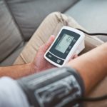 man doing a reading of his blood pressure with a blood pressure monitor while being seated on a couch at home